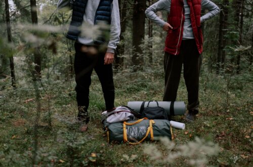 Ultralight foldable camping seat cushion beside hiking backpack on forest campsite ground